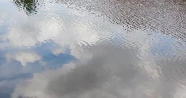 Su yüzeyi dalgaları dalgalanır mavi gökyüzündeki bulutları yansıtır