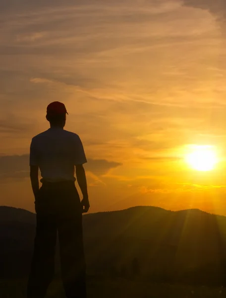 Silhouette eines jungen Mannes in den Bergen bei Sonnenuntergang — Stockfoto