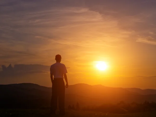 Młody człowiek na zielony trawnik w górach na zachodzie słońca Obrazy Stockowe bez tantiem