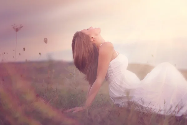 Beautiful girl is relaxing while sitting on field — Stock Photo, Image