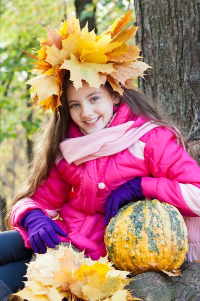 Girl in a wreath of maple leaves with pumpkin in autumn park — Stock Photo, Image