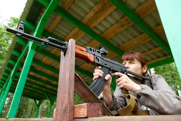 Young woman aiming at a target and shooting an automatic rifle f — Stock Photo, Image