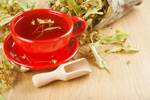 Xícara de chá de tília e flores em saco de lona na mesa de madeira — Fotografia de Stock