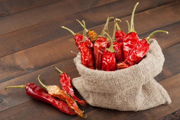 Red chili peppers in a canvas sack on wooden table — Stock Photo, Image