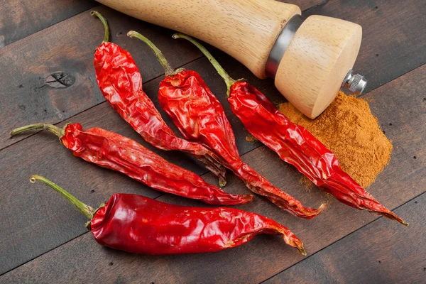 Chiles rojos, molino de pimienta y pila de tierra fría sobre mesa de madera — Foto de Stock