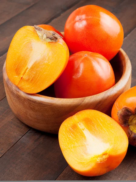 Persimmons in bowl on wooden table — Stock Photo, Image