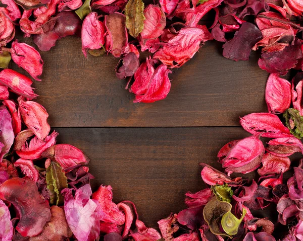 Flower Petals forming a heart shape against wooden background — Stock Photo, Image