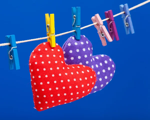 Dos corazones colgando en un tendedero con pinzas de ropa, fondo azul — Foto de Stock