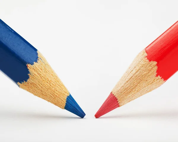 Red and blue pencils against each other on a white paper sheet — Stock Photo, Image