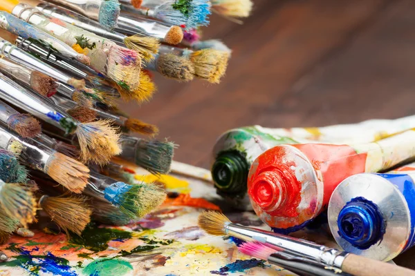 Art brushes, oil paint tubes, artist palette on wooden table — Stock Photo, Image