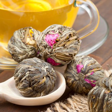 Green tea balls with flowers, tea cup and wooden spoon on kitche