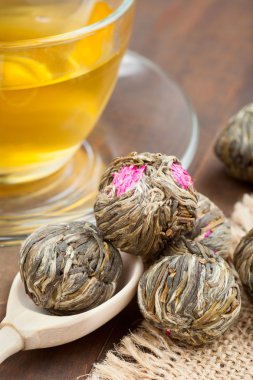 Green tea balls with flowers, tea cup and wooden spoon on kitche