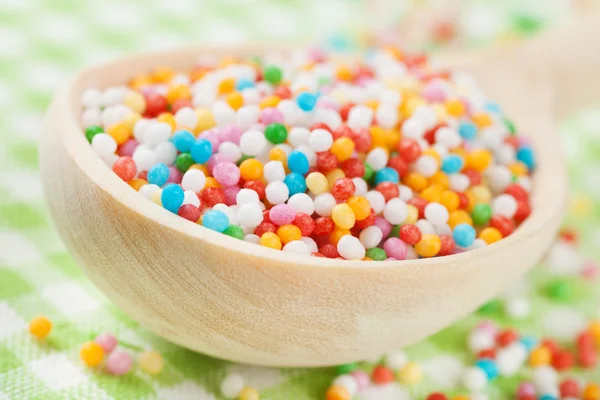 Polvilhas de açúcar coloridas em colher de madeira na toalha de mesa — Fotografia de Stock