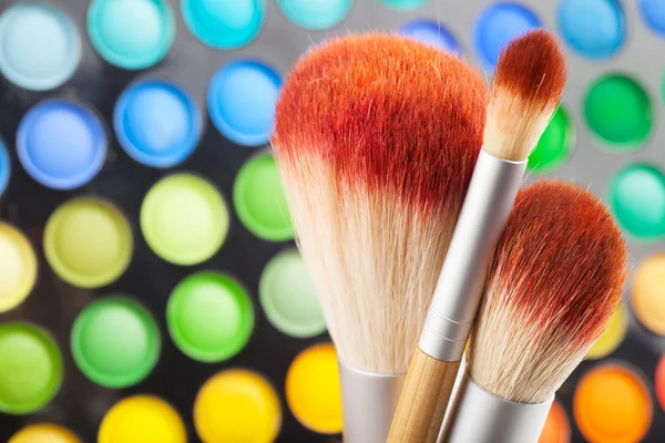 Pincéis de maquiagem e conjunto de sombras coloridas de olhos como fundo — Fotografia de Stock