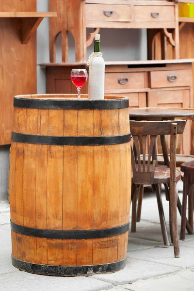 Tønne av tre med vin- og glassflasker, stol og bord i – stockfoto