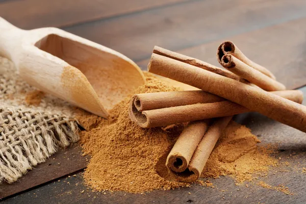 Varas de canela e pó de canela em colher de madeira, na mesa — Fotografia de Stock