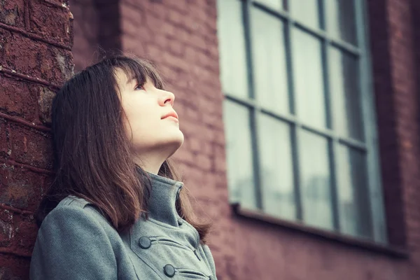 Pensive beautiful young girl standing near a brick wall — Stock Photo, Image