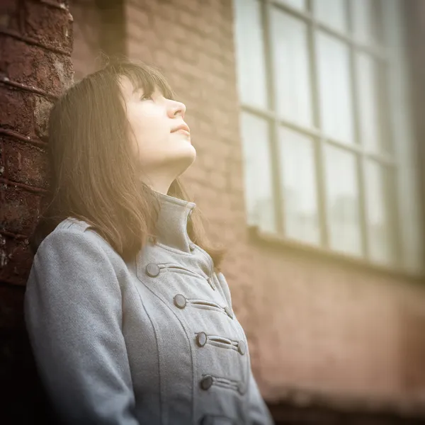 Young girl standing near a brick wall and looking up — Stock Photo, Image