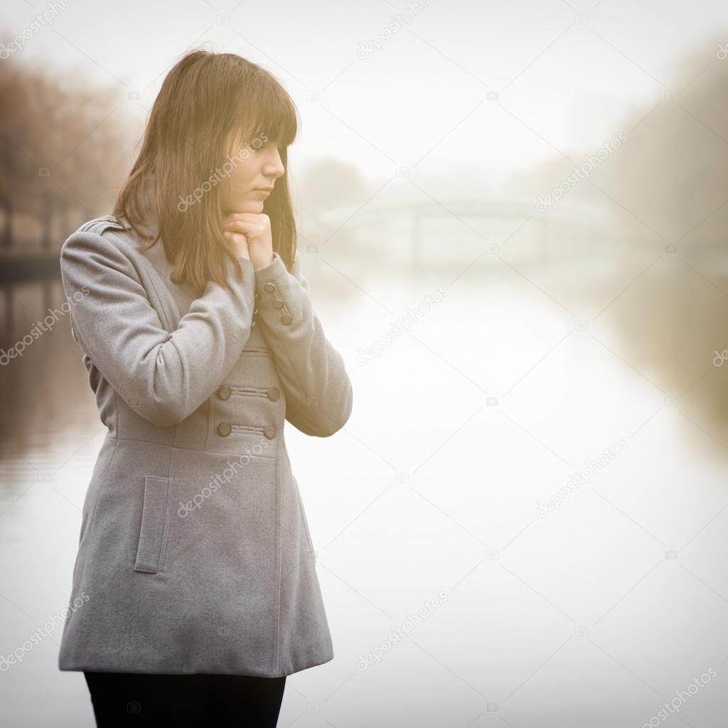 pretty sad girl in cold weather near river in a fog