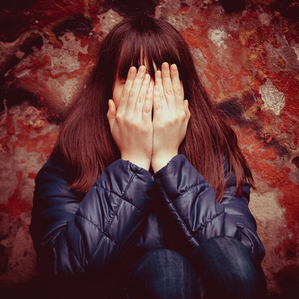 Girl with hands over eyes near wall outdoors