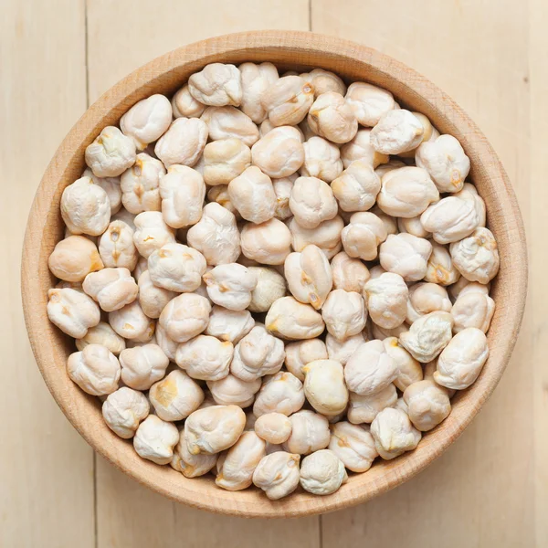 Chickpeas in wooden bowl, on wooden kitchen table — Stock Photo, Image