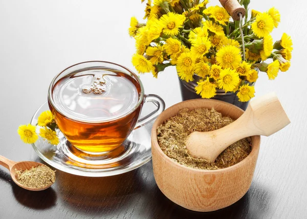 Chá saudável, balde com flores coltsfoot e argamassa na mesa — Fotografia de Stock