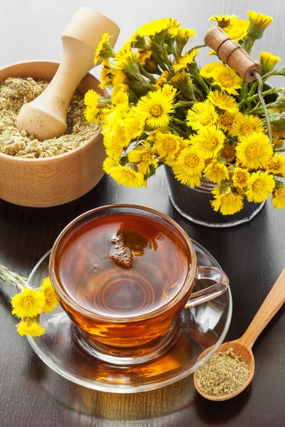 Chá saudável, balde com flores coltsfoot e argamassa na mesa — Fotografia de Stock