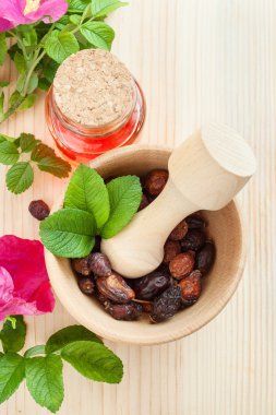 uçucu yağ, cam şişe, kurutulmuş kuşburnu meyveleri ahşap 