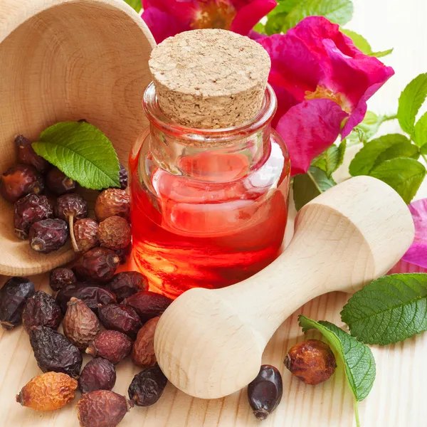 Ätherisches Öl in Glasflasche, getrocknete Hagebuttenbeeren in Holz — Stockfoto