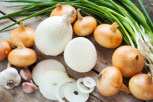 Different onions and garlic on wooden table — Stock Photo, Image