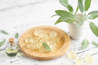 Boğaz ağrısı ve öksürük için bilge pastiller. Bir şişe adaçayı esaslı yağ ve salvia resmi yaprakları beyaz ahşap masaya konur..