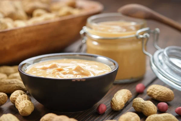 Bir kase fıstık ezmesi ve taze fındık. Arka planda çiğ organik fıstık ezmesi kavanozu..