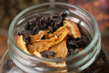 Aromatic black tea leaves with dried citrus slices and peel. Closeup of dry black tea with dried orange slices in an open glass jar for storing tea.
