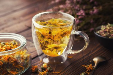 Sağlıklı bir bardak Calendula bitkisel çayı, bir kavanoz kurutulmuş takviyeli şifalı bitkiler ve ahşap masa üzerinde heather çiçekleri. Alternatif bitkisel ilaç.