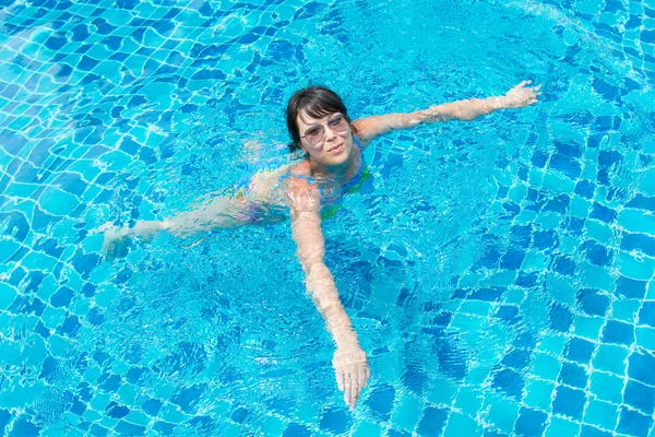 Beautiful young girl in sunglasses floating in the pool — Stock Photo, Image