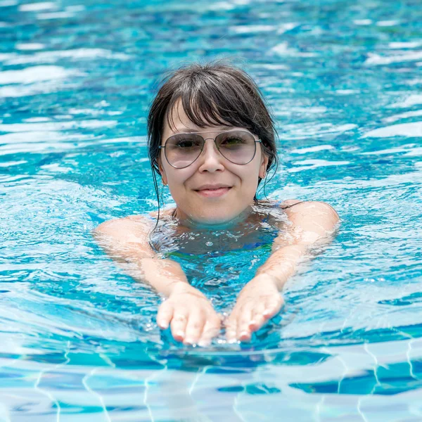 Beautiful young girl in sunglasses floating in the pool — Stock Photo, Image