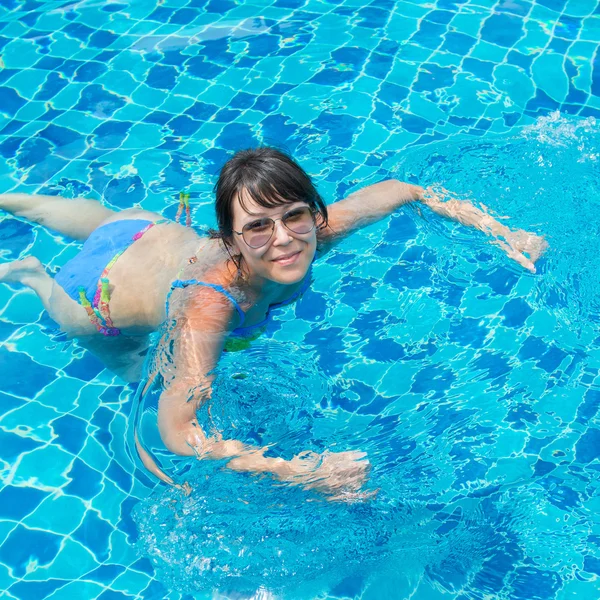 Schönes junges Mädchen mit Sonnenbrille, das im Pool schwimmt — Stockfoto