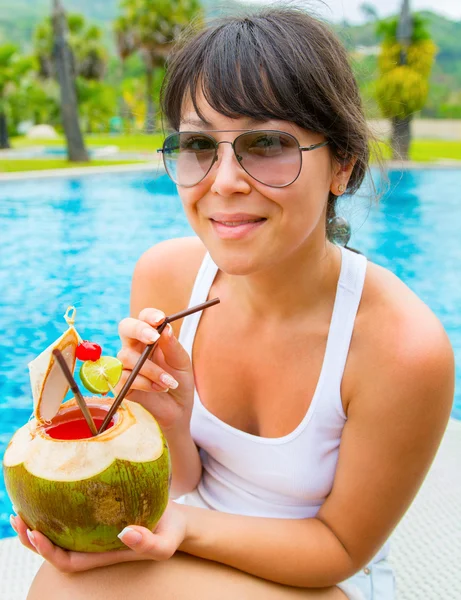 Vacker kvinna dricka kokosnöt cocktail mot utomhuspool — Stockfoto