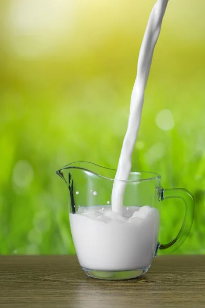 Γάλα που ρίχνει στο ποτήρι σε φόντο φύση — Φωτογραφία Αρχείου