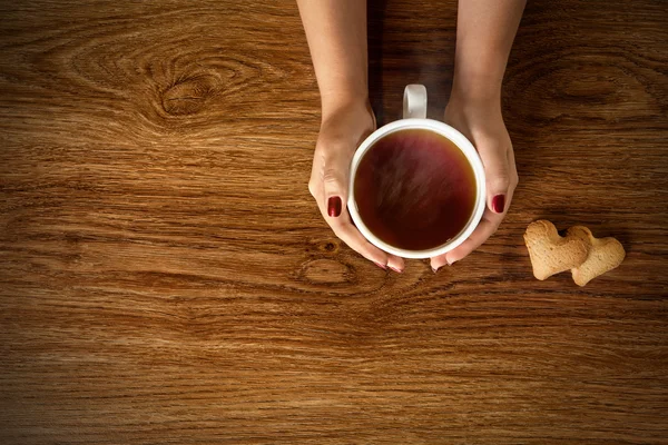 Kobieta trzyma filiżankę gorącej herbaty z plików cookie na drewnianym stole — Zdjęcie stockowe