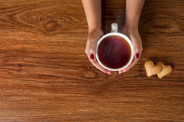 Žena držící šálek horkého čaje s cookies na dřevěný stůl — Stock fotografie