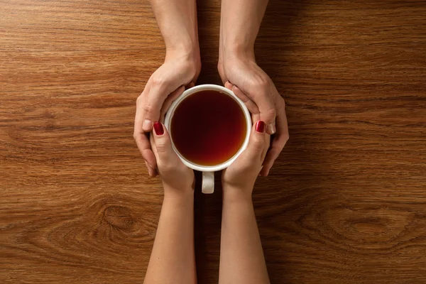 Frau hält heißen Tee mit Keksen auf Holztisch — Stockfoto