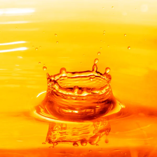 Drop falling into orange water with splash — Stock Photo, Image