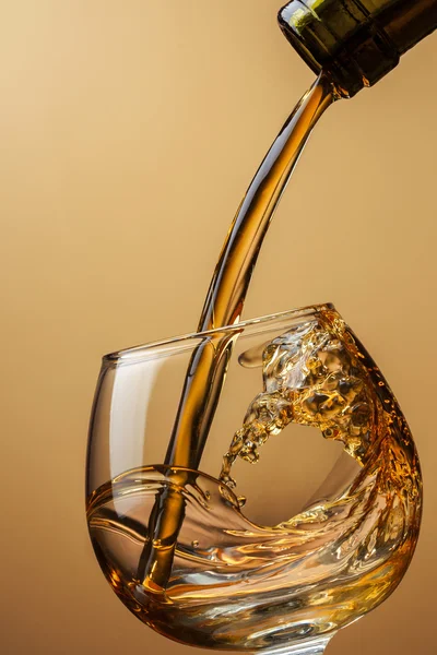 Coñac vertiendo de botella en vidrio con salpicadura en respaldo marrón — Foto de Stock