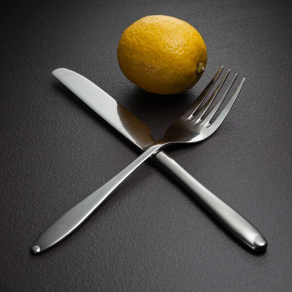 Zitrone mit gekreuzten Messer und Gabel auf schwarz — Stockfoto