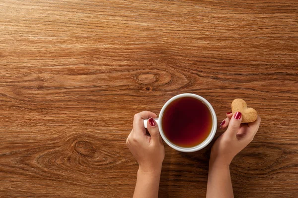Mujer sosteniendo taza de té caliente con galletas — Foto de Stock