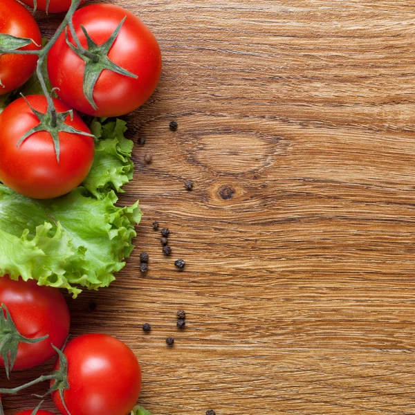 Tomates rojos con ensalada verde sobre madera — Foto de Stock