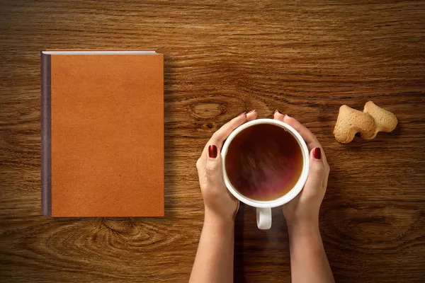 Mulher com xícara de chá, biscoitos e livro — Fotografia de Stock
