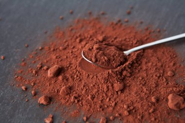 Çay kaşığının yukarısından, gri arka planda koyu kahverengiye boyanmış kakao tozu yığınına yerleştirilmiş.