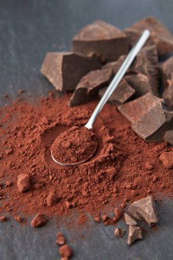 Yukarıdan gelen organik siyah acı kakao tozu çay kaşığı ve gri arka planda bir yığın çikolata.